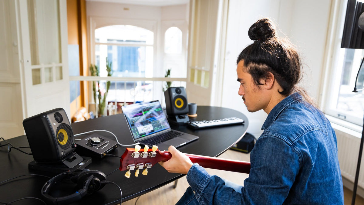 Musician at a desk in a bright home studio with KRK monitors, laptop and audio interface